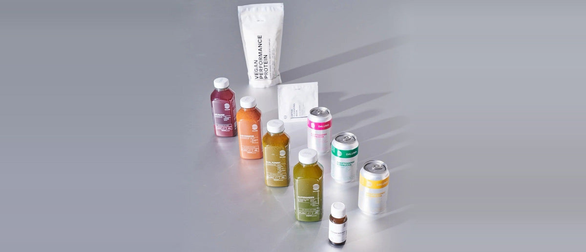 Smartphone mit dem DALUMA Health Coach Chat vor kaltgepressten Säften, Kombucha und Detox Clearing Mask.