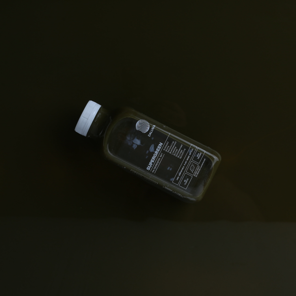 Eine Kunststoffflasche mit weißem Verschluss, die teilweise mit einer dunkelgrünen Flüssigkeit gefüllt ist, liegt auf einer dunklen Fläche. Das Etikett auf der Flasche ist sichtbar und enthält Text und ein Logo.