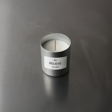 Eine weiße DUFTKERZE GRADE 0.1 RELIEVE von Nullpunkt in einem mattsilbernen Behälter ruht auf einer glatten grauen Oberfläche - ideal für Entspannung und Aromatherapie.