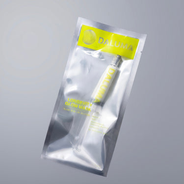 Eine DALUMA LONGEVITY GLOW MASKE – eine Peel-off-Gesichtsmaske für die Netzhaut in einem spritzenartigen Behälter, versiegelt in einem transparenten Plastikbeutel mit gelbem Logo.