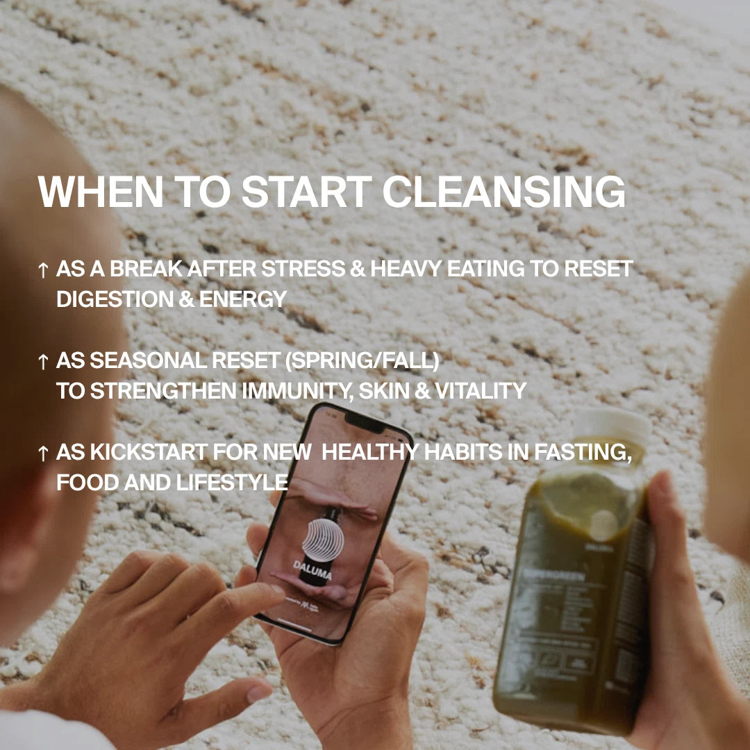 Eine Person sitzt auf einem hellen Teppich, hält einen grünen Saft und ein Smartphone mit dem DALUMA-Bildschirm. Das Bild zeigt, wann man mit der BESSERE SAFTKUR 7 TAGE von DALUMA beginnen sollte, um die Verdauung, das Immunsystem und gesunde Gewohnheiten zu verbessern.