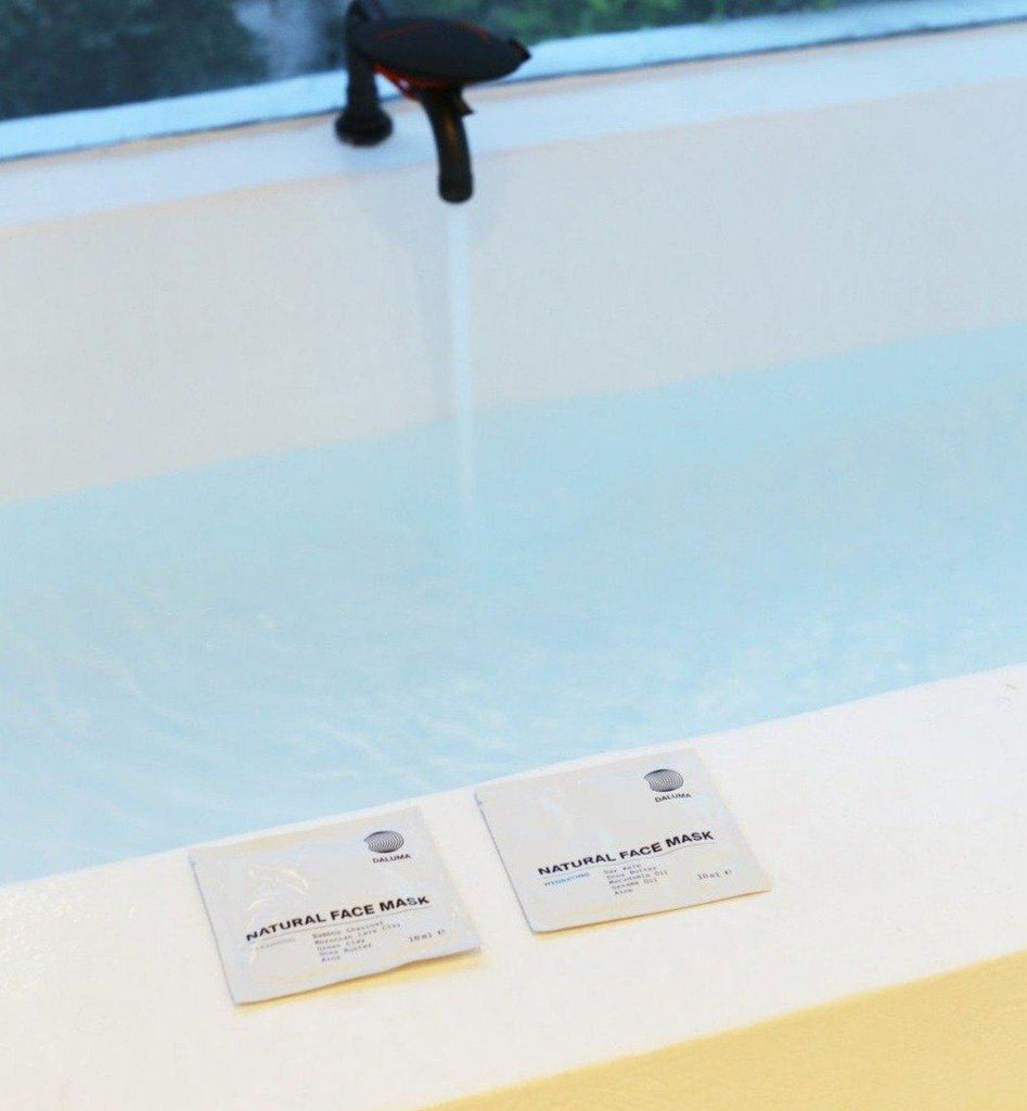 Im Hintergrund füllt sich eine Badewanne, während zwei DALUMA DEEP HYDRATION FEUCHTIGKEITSMASKE-Pakete - mit feuchtigkeitsspendenden Eigenschaften und natürlichen Zutaten - auf dem Wannenrand in einer entspannenden, spaähnlichen Atmosphäre ruhen.
