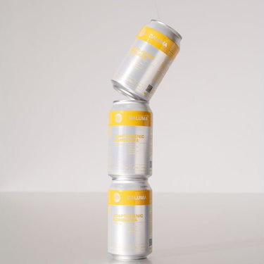 Drei silber-gelbe DALUMA GINGER GUN INGWER KOMBUCHA-Dosen aus dem 24er-Pack sind senkrecht gestapelt, wobei die oberste Dose auf zwei aufrecht stehende Dosen gekippt ist, vor einem schlichten Hintergrund. Genieße erfrischenden Geschmack mit probiotischen Kulturen.