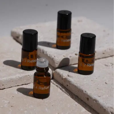 Vier kleine Braunglasflaschen mit schwarzen Verschlüssen sind auf hellen Steinfliesen angeordnet. Eine Flasche ist offen und zeigt einen Tropfverschluss, während die anderen geschlossen sind. Die Flaschen sind mit Nummern und Text beschriftet.