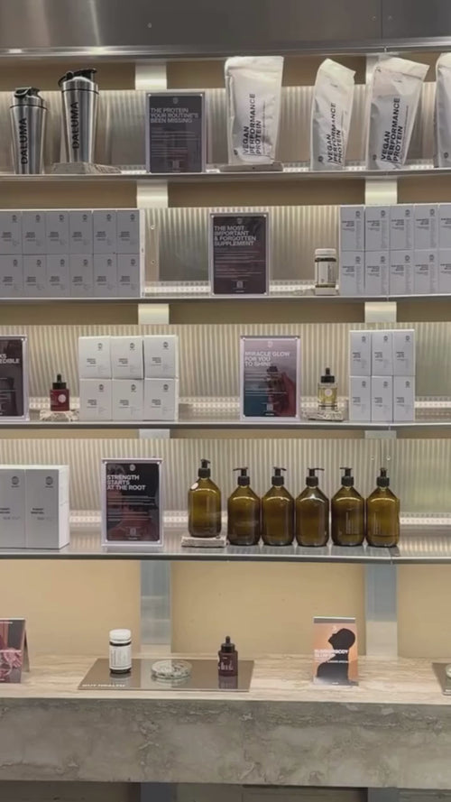 Ein modernes Café mit einem Schild mit der Aufschrift DALUMA über dem Tresen. Zwei Personen sitzen auf Hockern an der Theke, die eine trägt eine karierte Jacke, die andere hat lange Haare. Man sieht runde Regale und Küchengeräte.