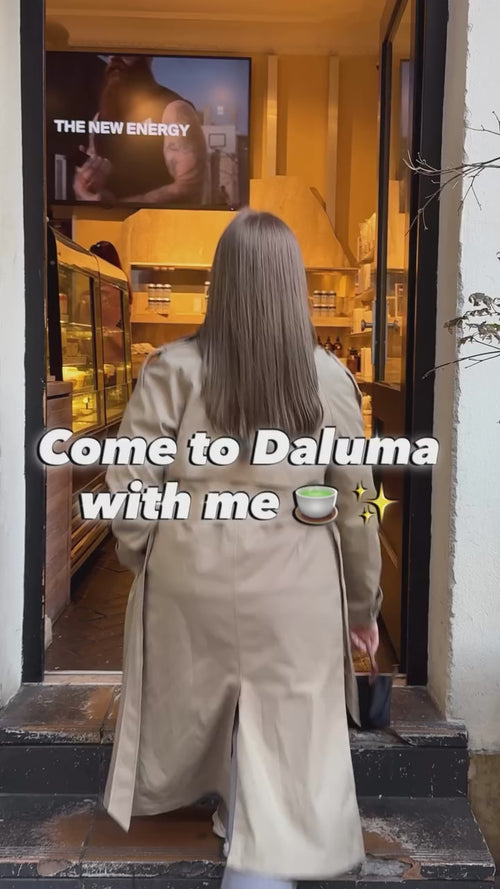 Ein weißes Schild mit einem kreisförmigen schwarzen Linienmuster hängt vor einem Gebäude. Der Schriftzug Clean Breakfast at Daluma ist über das Bild gelegt. In der unteren linken Ecke ist etwas Laub zu sehen.