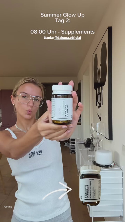 Eine Frau mit Brille hält in einem modernen, hellen Raum zwei Nahrungsergänzungsmittelflaschen in die Kamera. Der Text über ihr lautet: "Summer Glow Up Tag 2: 08:00 Uhr - Nahrungsergänzungsmittel". Ein Pfeil zeigt auf eine weitere Flasche mit Nahrungsergänzungsmitteln auf einer Theke.