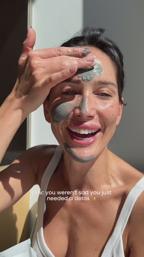 Eine lächelnde Frau trägt eine graue Gesichtsmaske auf ihre Stirn und Wangen auf. Sonnenlicht scheint auf ihr Gesicht. Der Text auf dem Bild besagt, pov: Du warst nicht traurig, du brauchtest nur eine Entgiftung ✨.