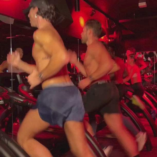 Menschen ohne Hemd trainieren auf Laufbändern unter roten Lichtern, die Energie und Bewegung einfangen - eine intensive Szene in Dalumas HEALTH CLUB PRO MEMBERSHIP Fitnessstudio.